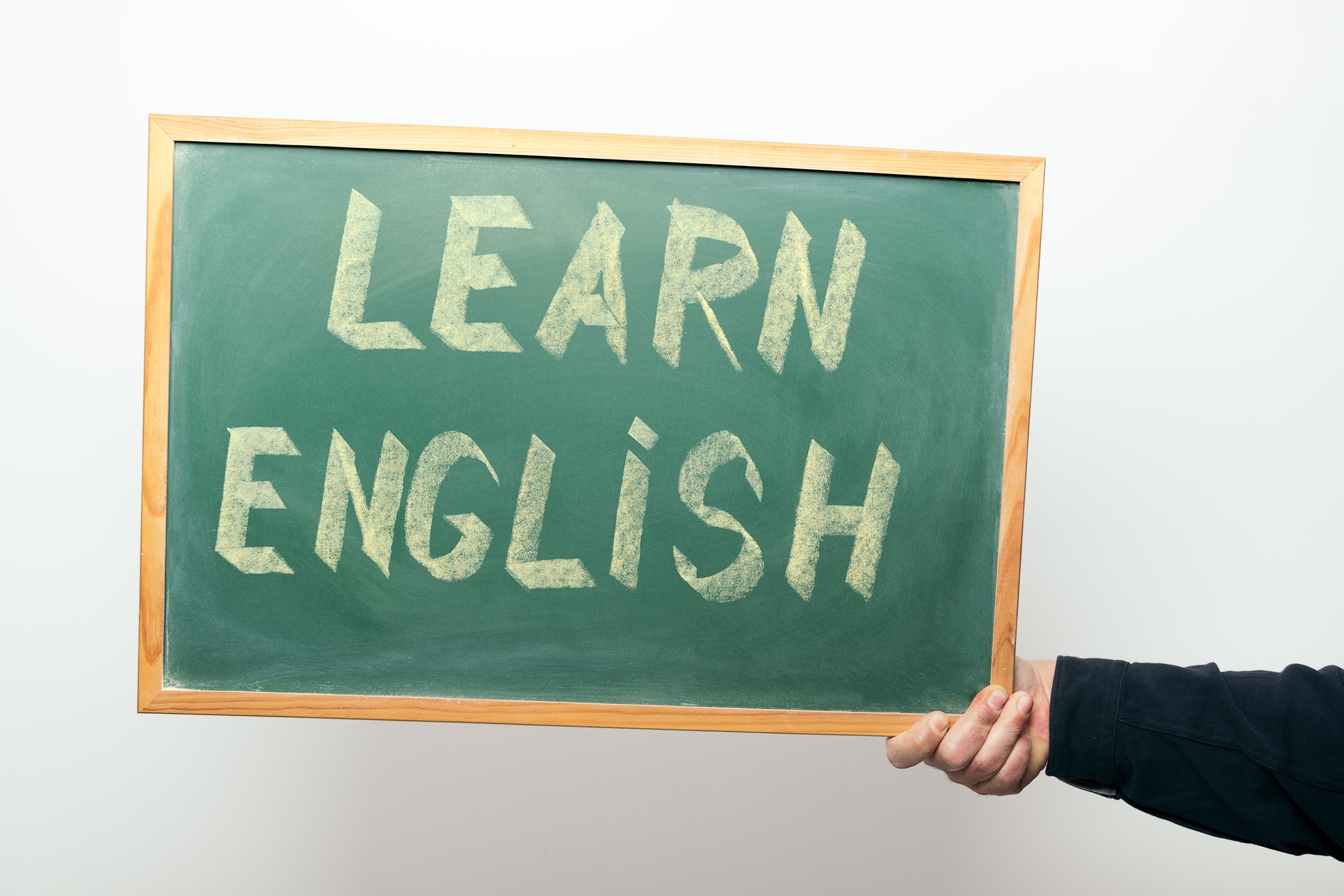 Зеленая доска с надписью "LEARN ENGLISH", держимая рукой.